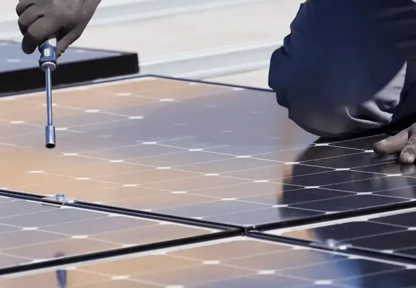 Mãos com chave apertando a fixação de uma placa solar durante manutenção